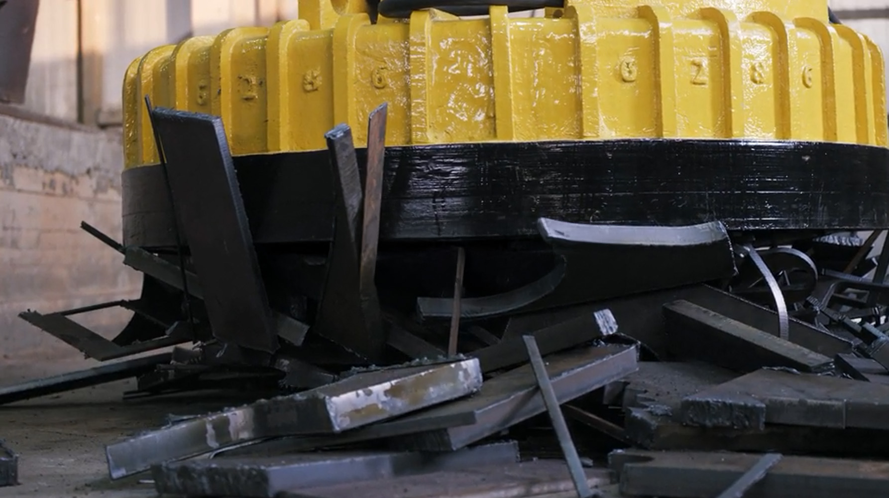 Ein großer, gelb-schwarz lackierter Elektromagnet hebt Metallplatten und Stahlteile in einer Lagerhalle an.